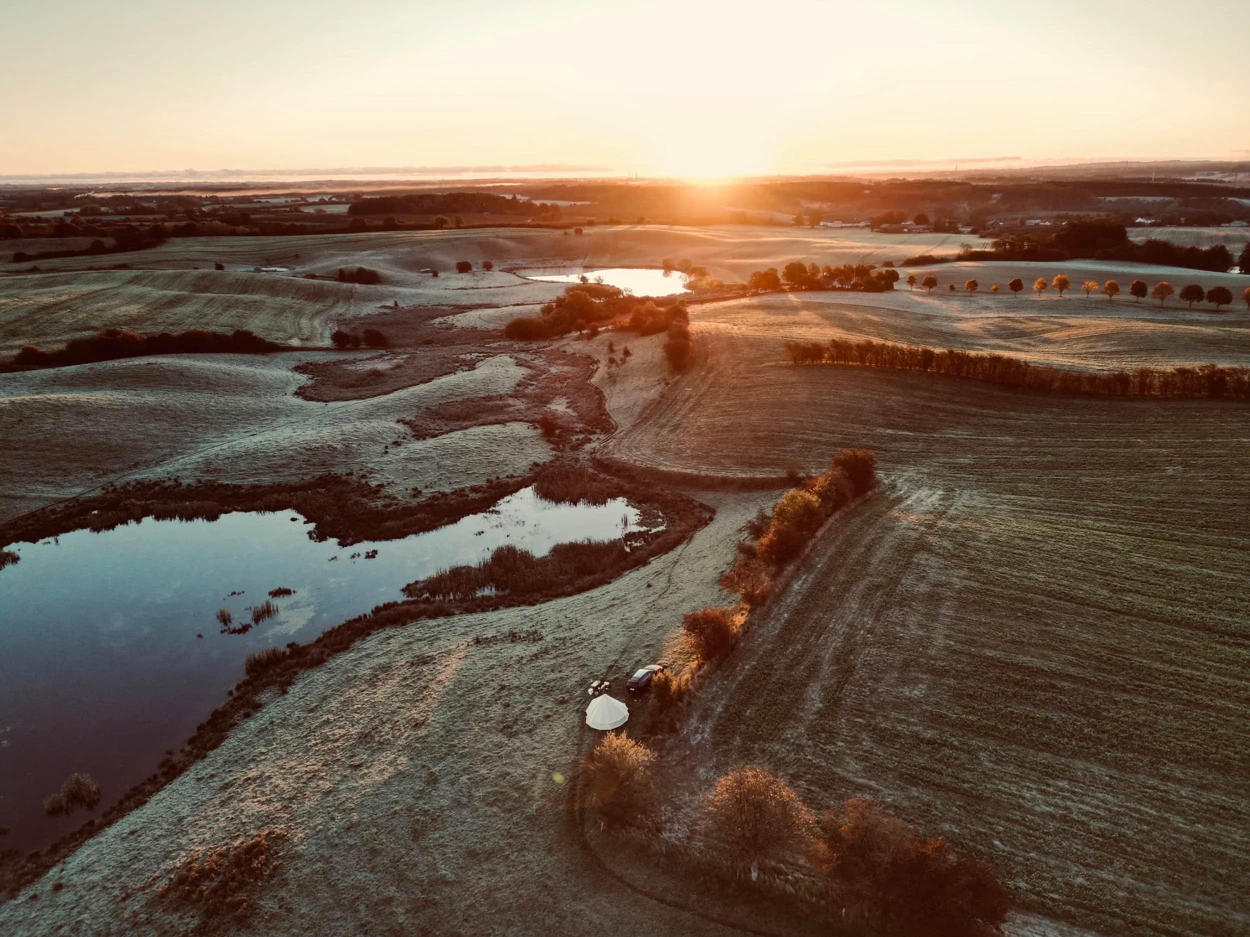 Luftfoto af en sø og marker i lav sol.